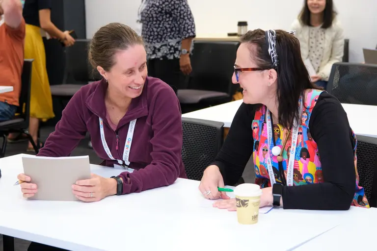 Two She Sharp participants collaborating over a tablet at a table during a 2023 event.