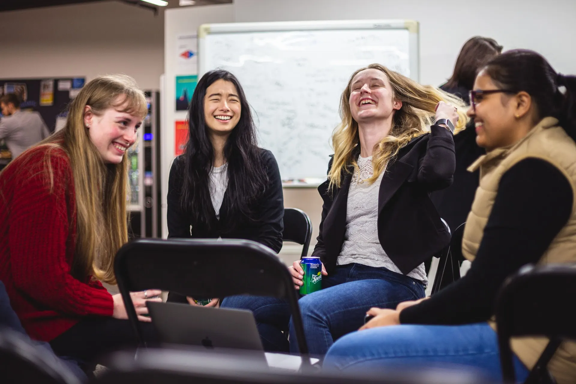 Four young women laughing together while seated during a She Sharp event.