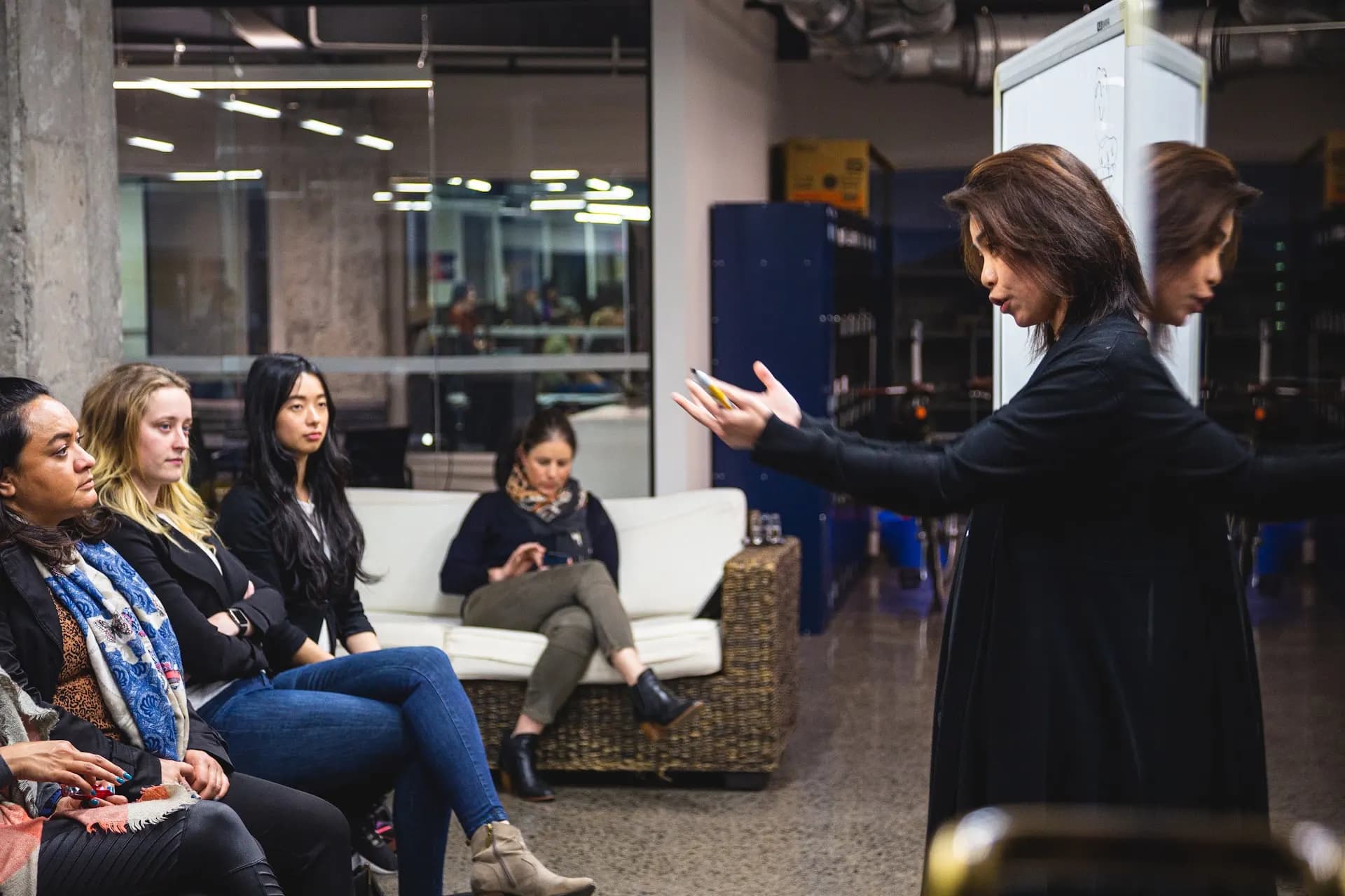 A speaker gesturing while addressing a small group seated on couches during an intimate She Sharp fireside session.