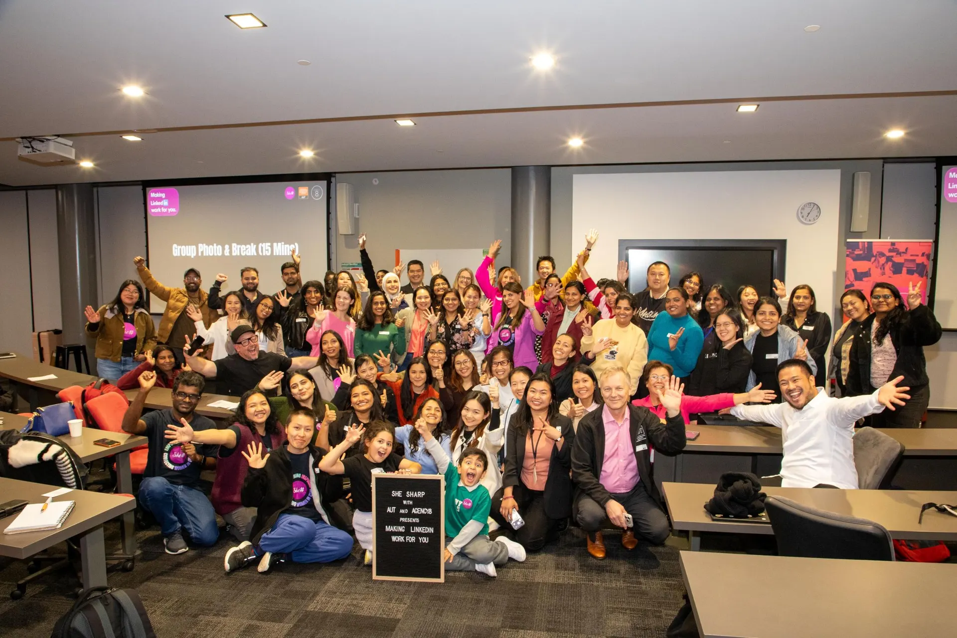 A room full of She Sharp attendees cheering with their hands raised in celebration.