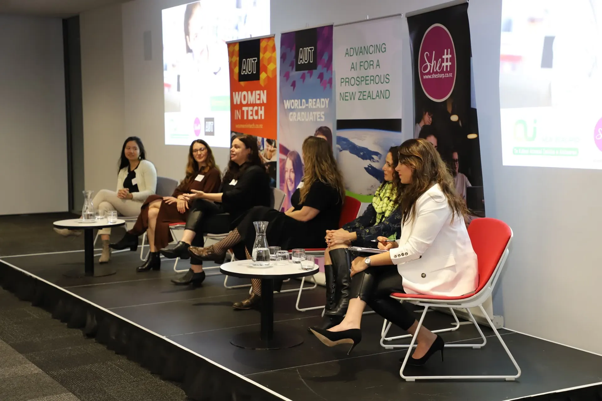 Panellists in conversation on stage during a She Sharp women in tech discussion.