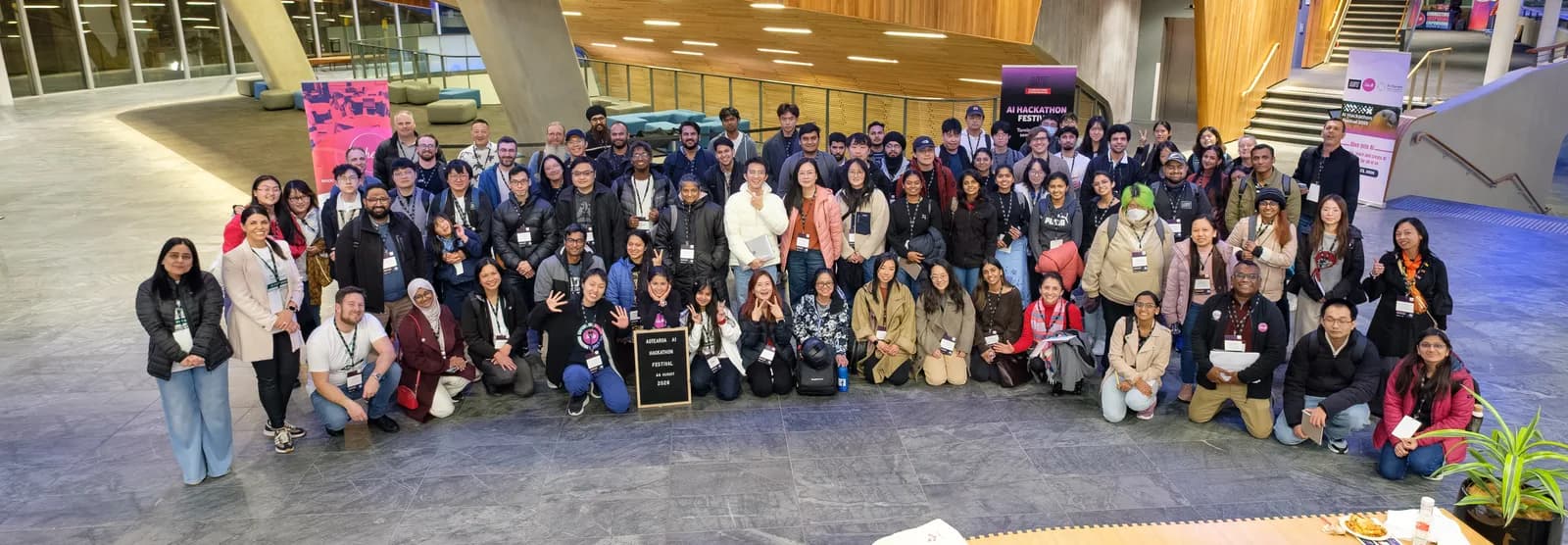 The whole festival gathered for a group photograph in the campus atrium, some kneeling at the front around a chalkboard sign.