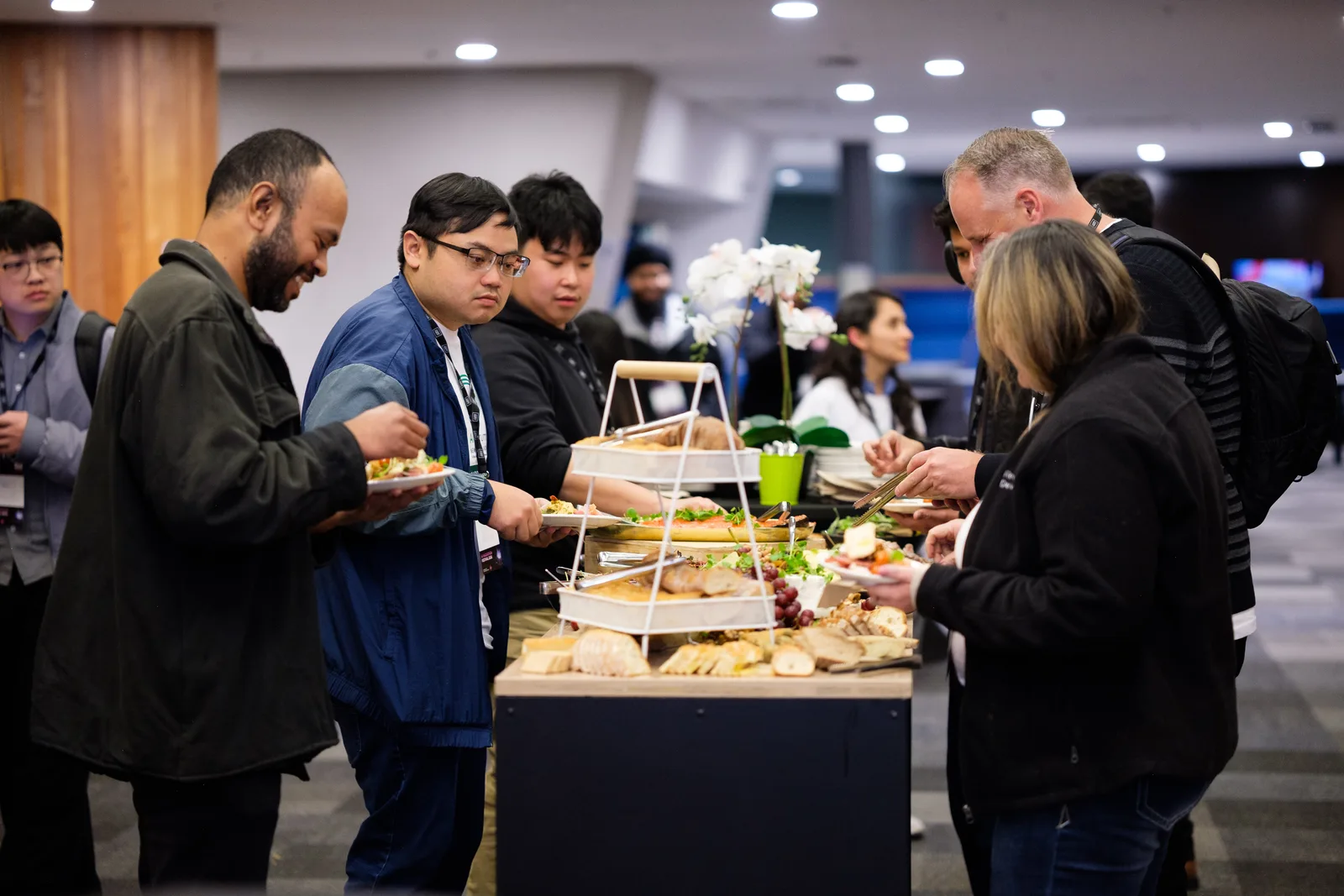 Attendees help themselves from a tiered catering stand during the break, plates in hand and conversation running across the table.