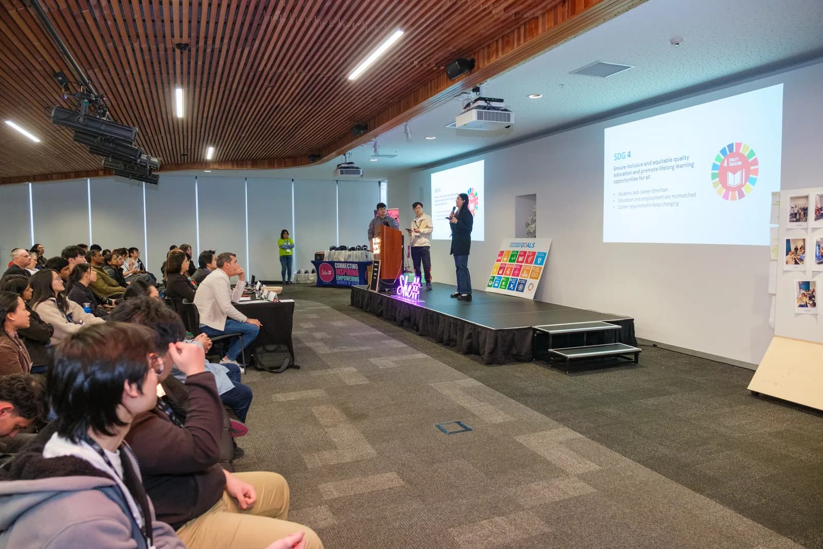 A full room seated in front of the stage watching a team present its solution on the big screen