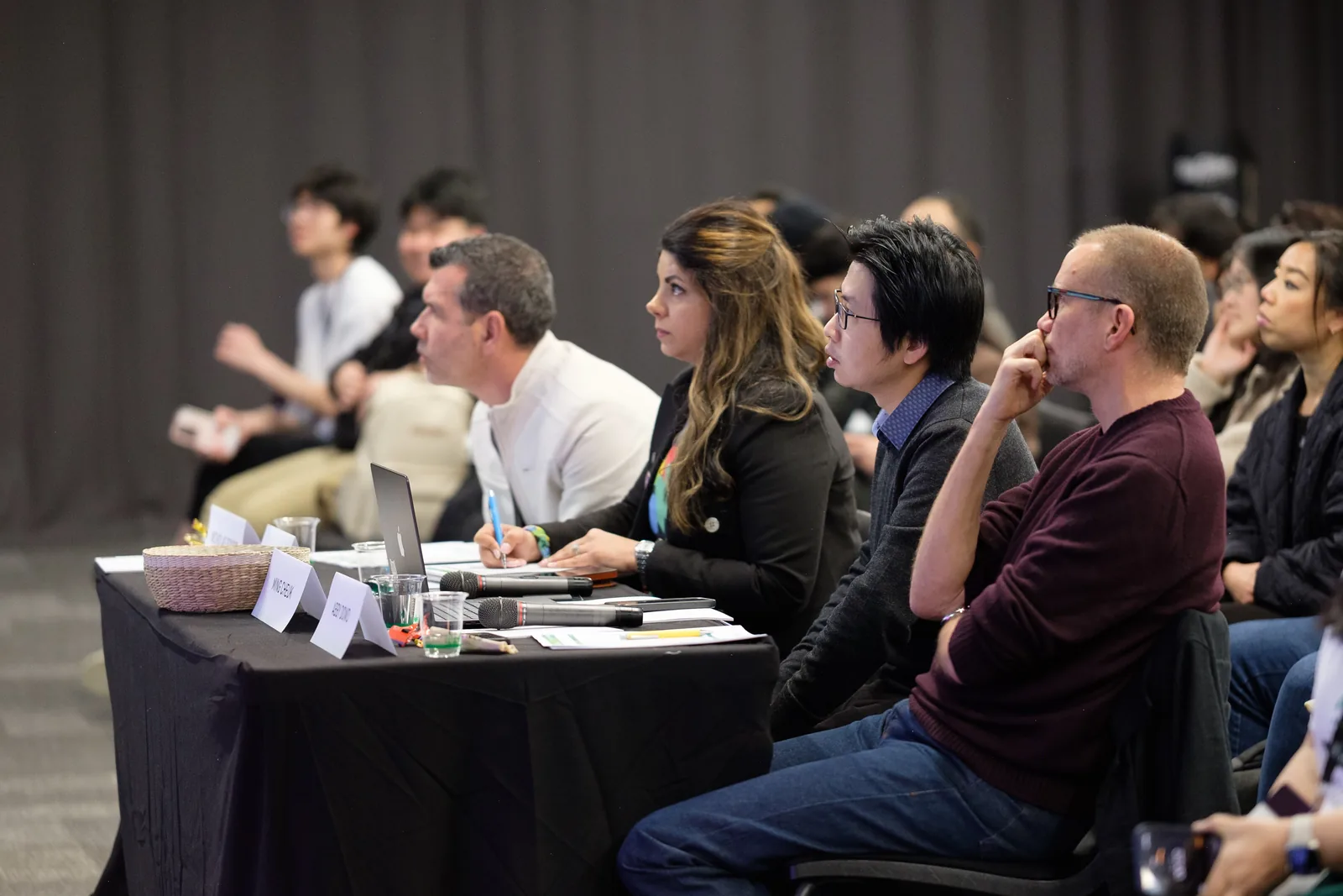 The judging panel seated at a long table, listening and taking notes during the final pitches