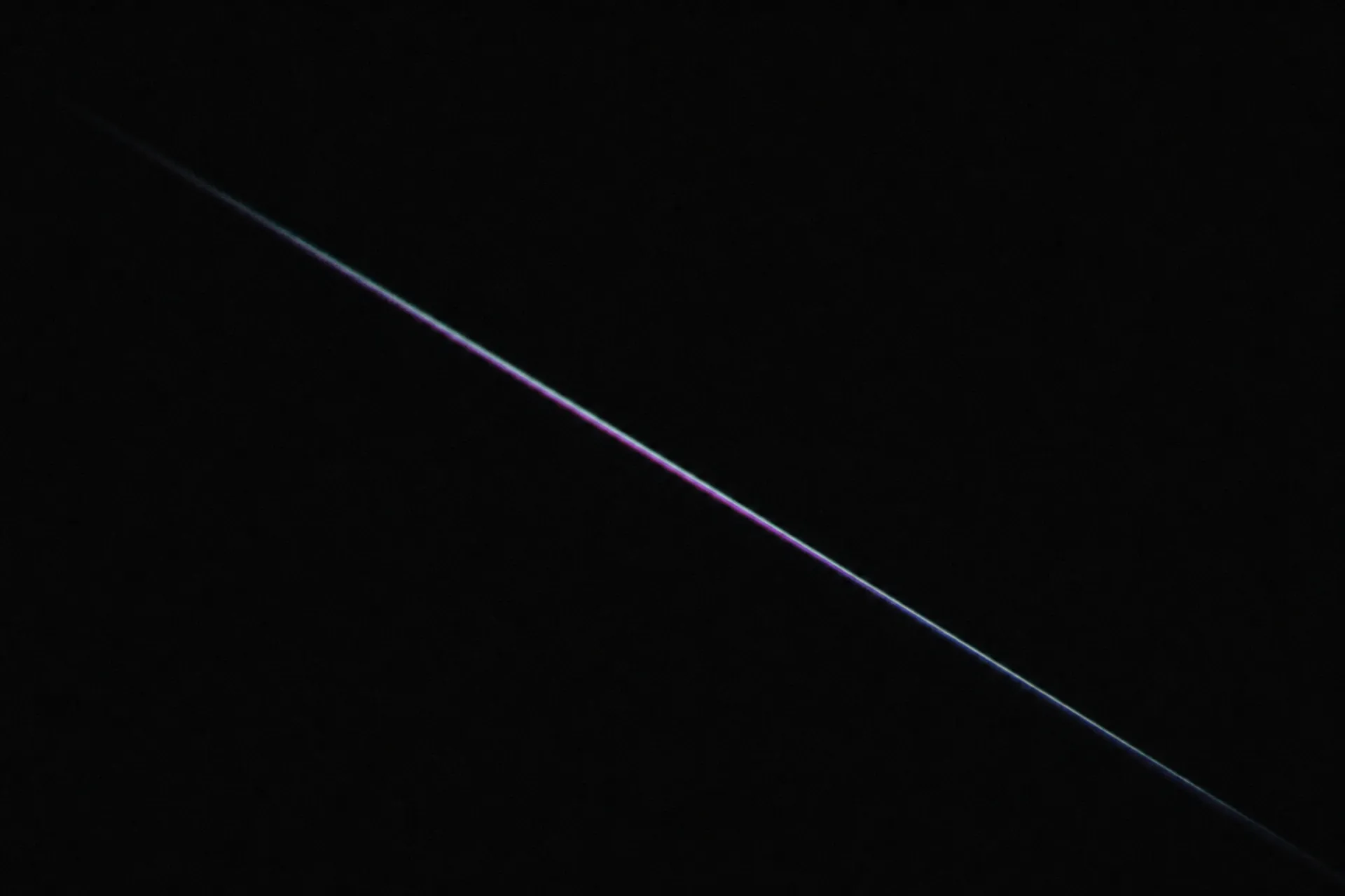 A single thin blade of refracted light crossing a black field on a steep diagonal.