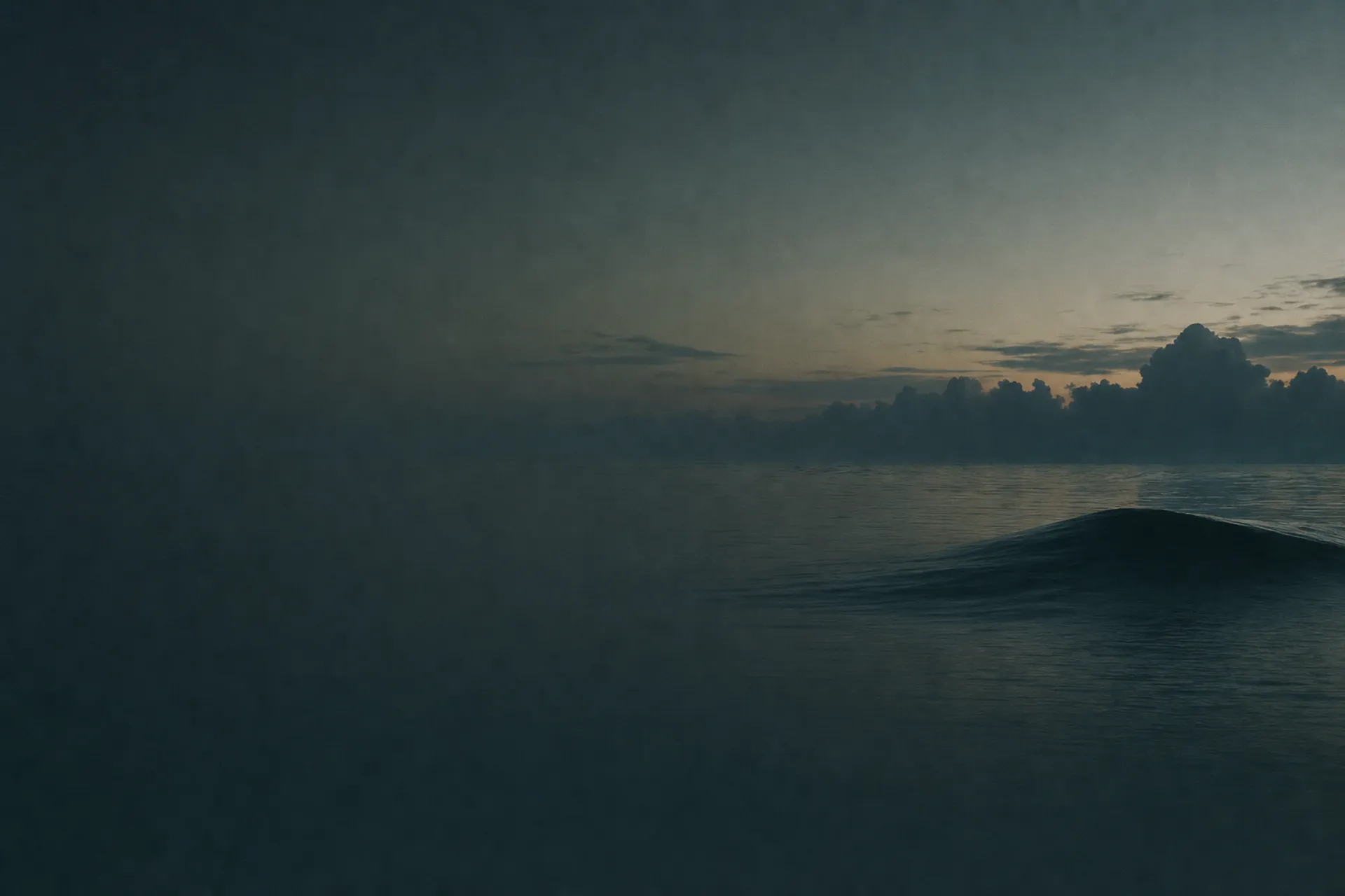 A calm dark sea at first light, the water deep greenstone green, one slow swell rising on the right beneath low cloud.